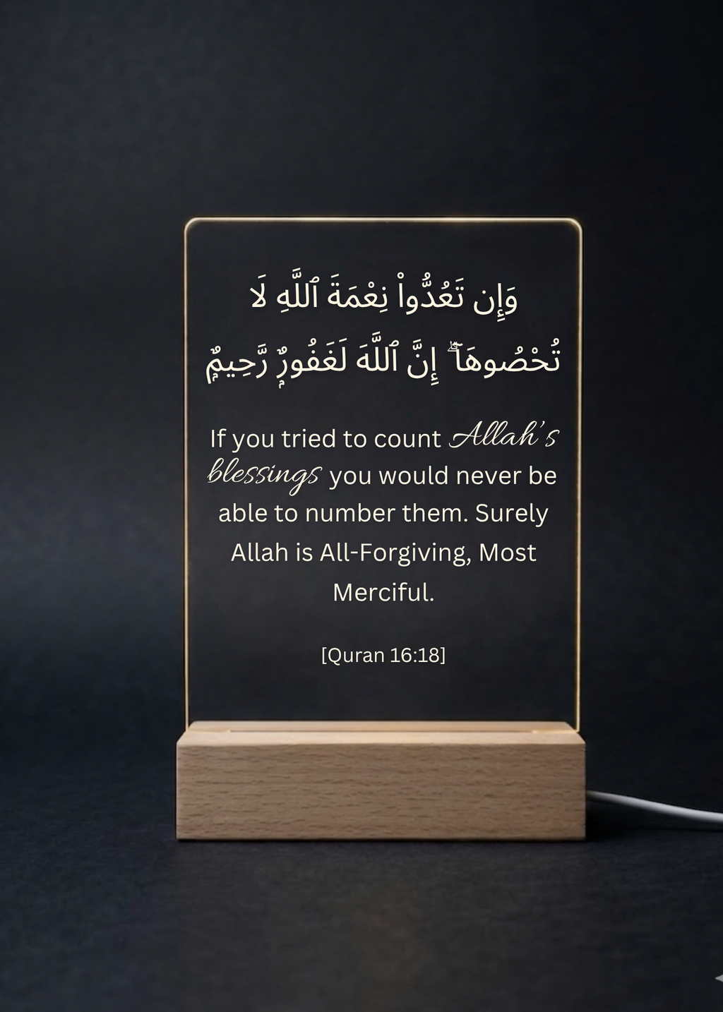 Acrylic plaque with Arabic and English text on a wooden stand against a dark background