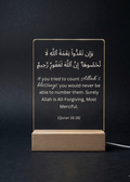 Acrylic plaque with Arabic and English text on a wooden stand against a dark background