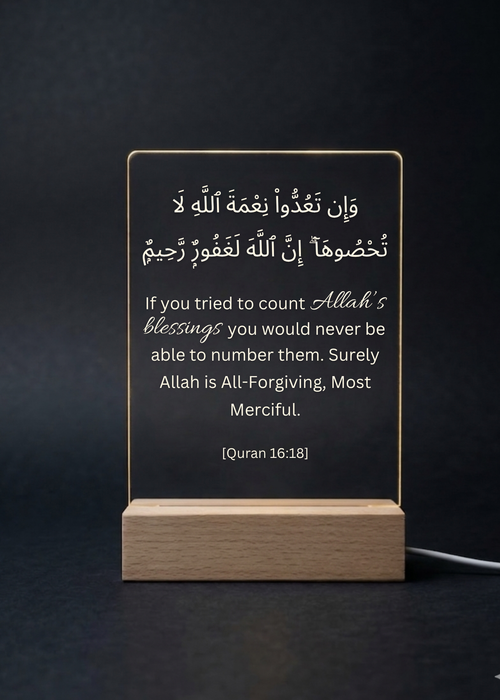 Acrylic plaque with Arabic and English text on a wooden stand against a dark background