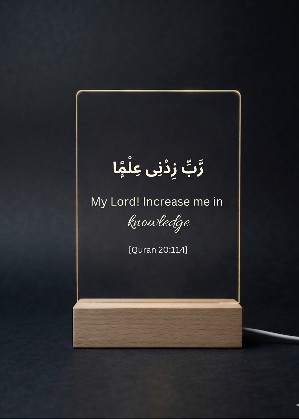 Acrylic sign with Arabic text and English translation on a wooden stand against a dark background