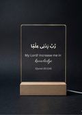 Acrylic sign with Arabic text and English translation on a wooden stand against a dark background