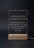Acrylic sign with Quran verse on a wooden stand against a dark background