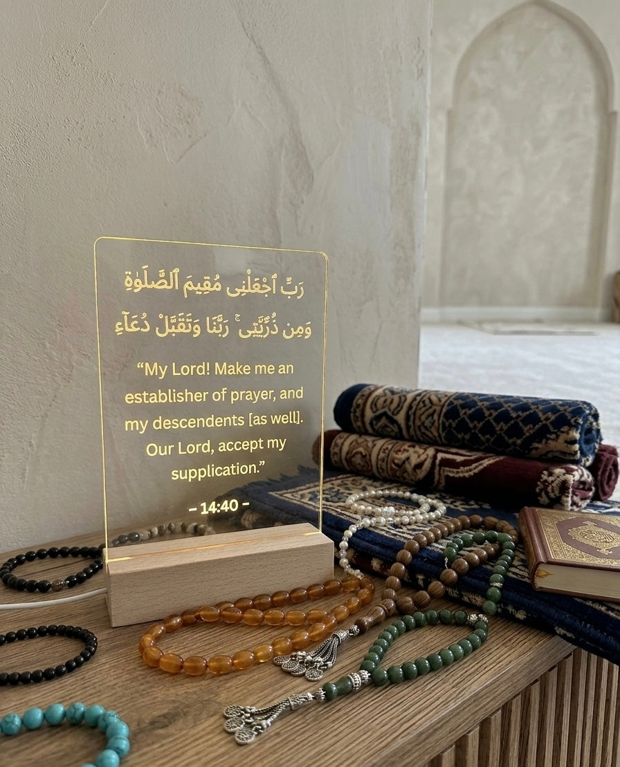 Decorative setup with prayer beads, tasbih, and a clear plaque with Arabic text on a wooden surface.