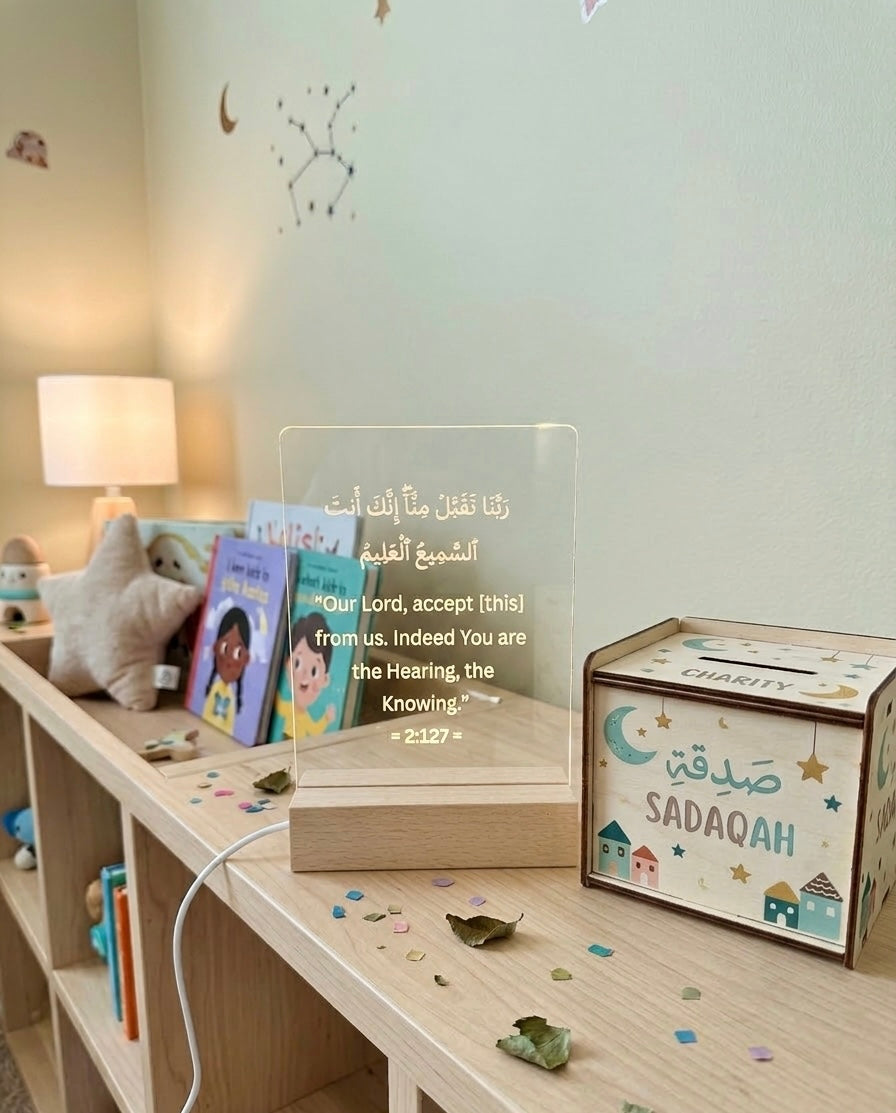 Acrylic LED sign on a wooden shelf with children's books and a small box labeled 'Sadaqah' in a room setting.