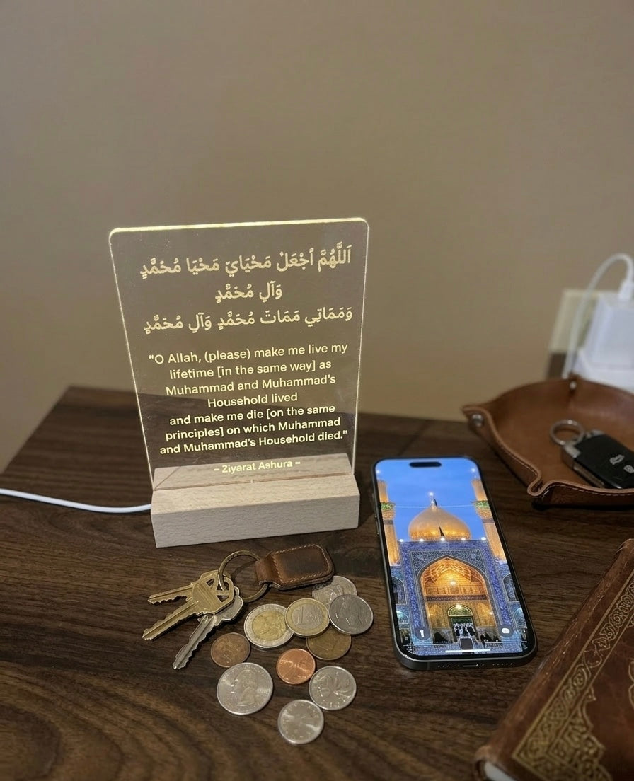 Lamp with Arabic text on a wooden surface with coins, keys, and a phone displaying an image of a mosque.