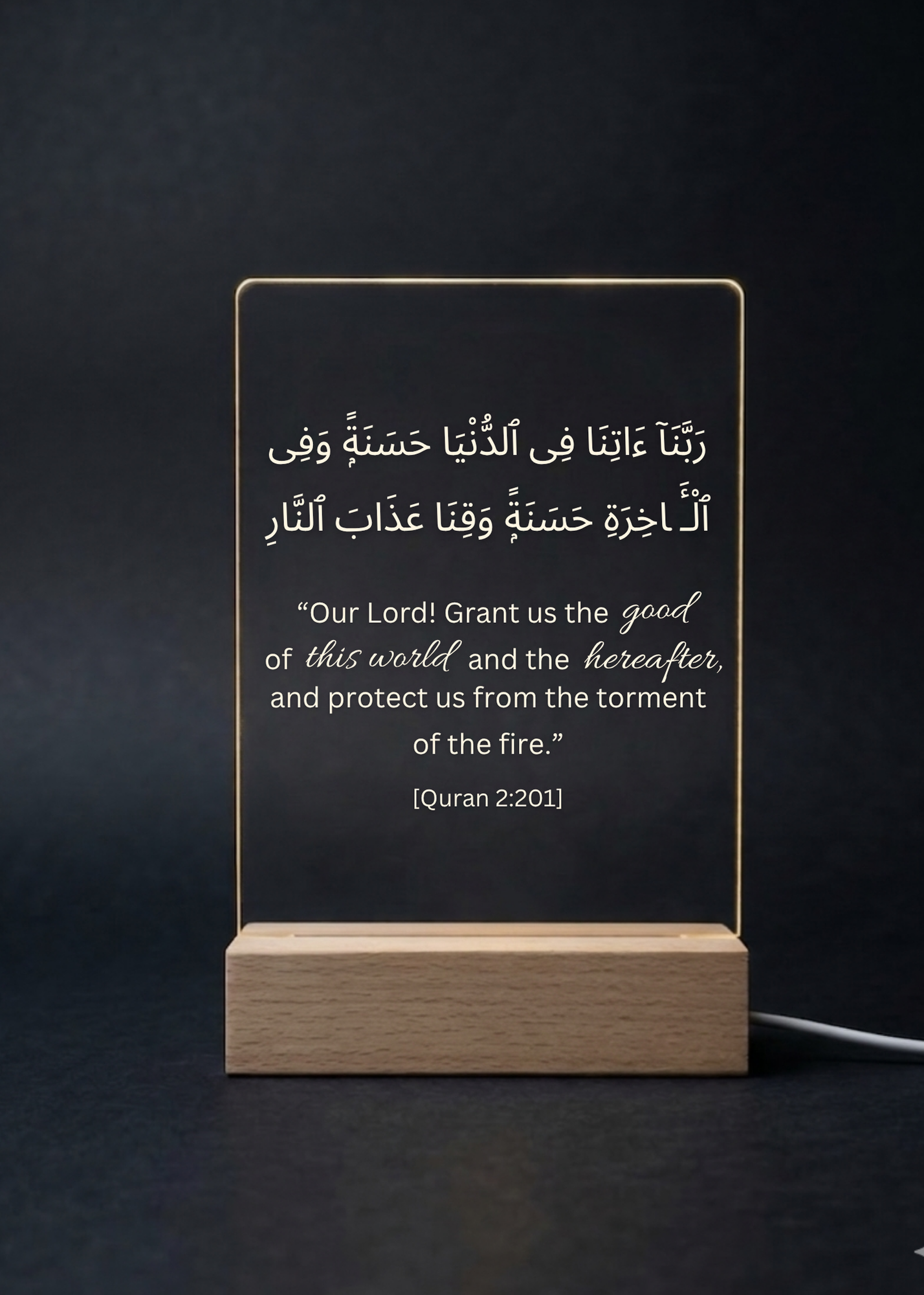 Acrylic plaque with Arabic text and English translation on a wooden stand against a dark background