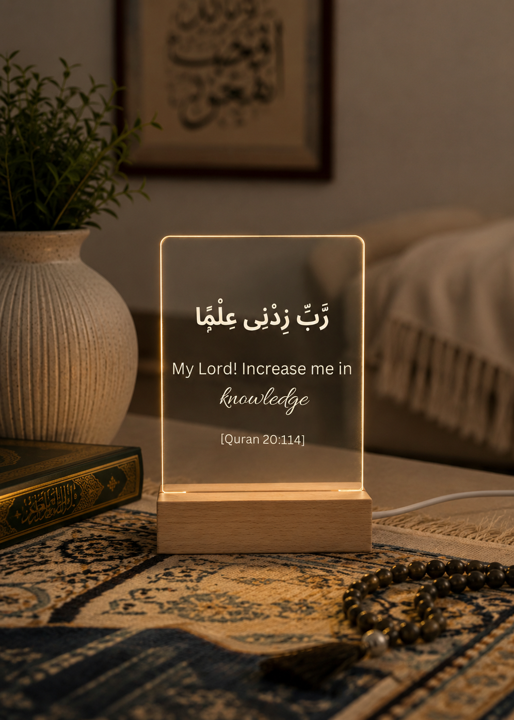 Decorative lamp with Arabic text and English translation on a table with a plant and books in the background.