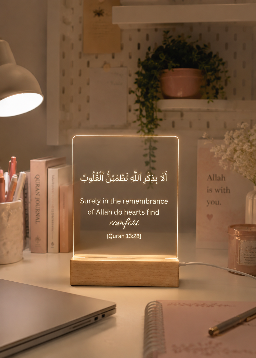 Decorative LED sign with Arabic text on a desk with books and a lamp.