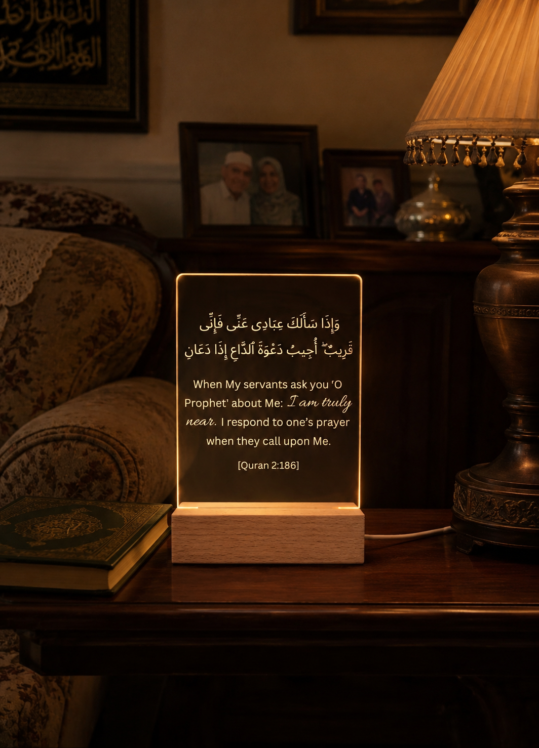 Lighted wooden plaque with Arabic text on a table in a dimly lit room.